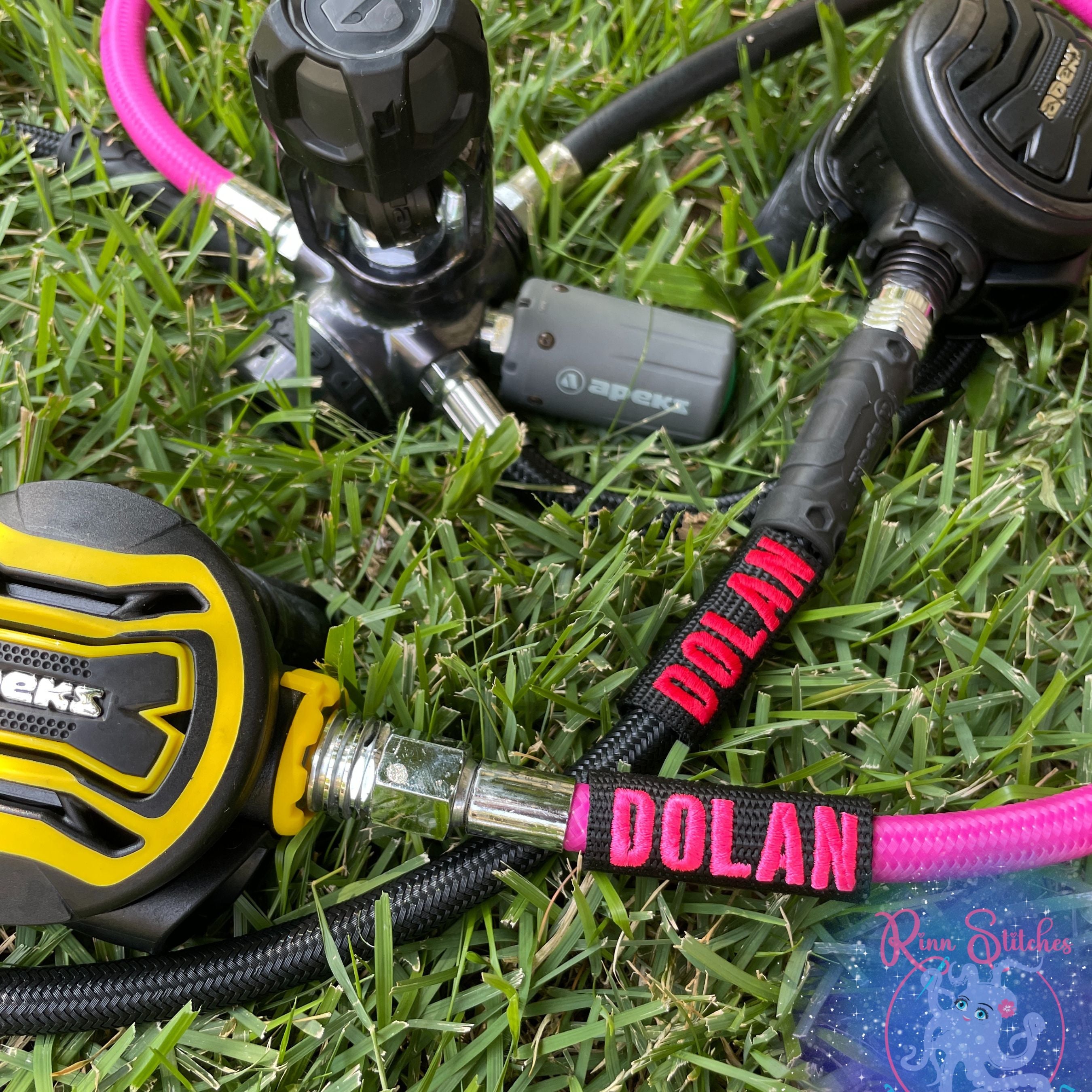 Scuba Diving Regulator Tags featuring the name Dolan in Red and Neon Pink attached to regulator hoses. Made by Rinn Stitches on Maui, Hawaii