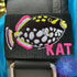 Personalized Clown Triggerfish BCD Tag with 'Kat' embroidered in Font #2 Aloha Beaches thread in Fuchsia pink, featuring black polka-dotted triggerfish design on black webbing with Velcro closure by Rinn Stitches on Maui, Hawaii