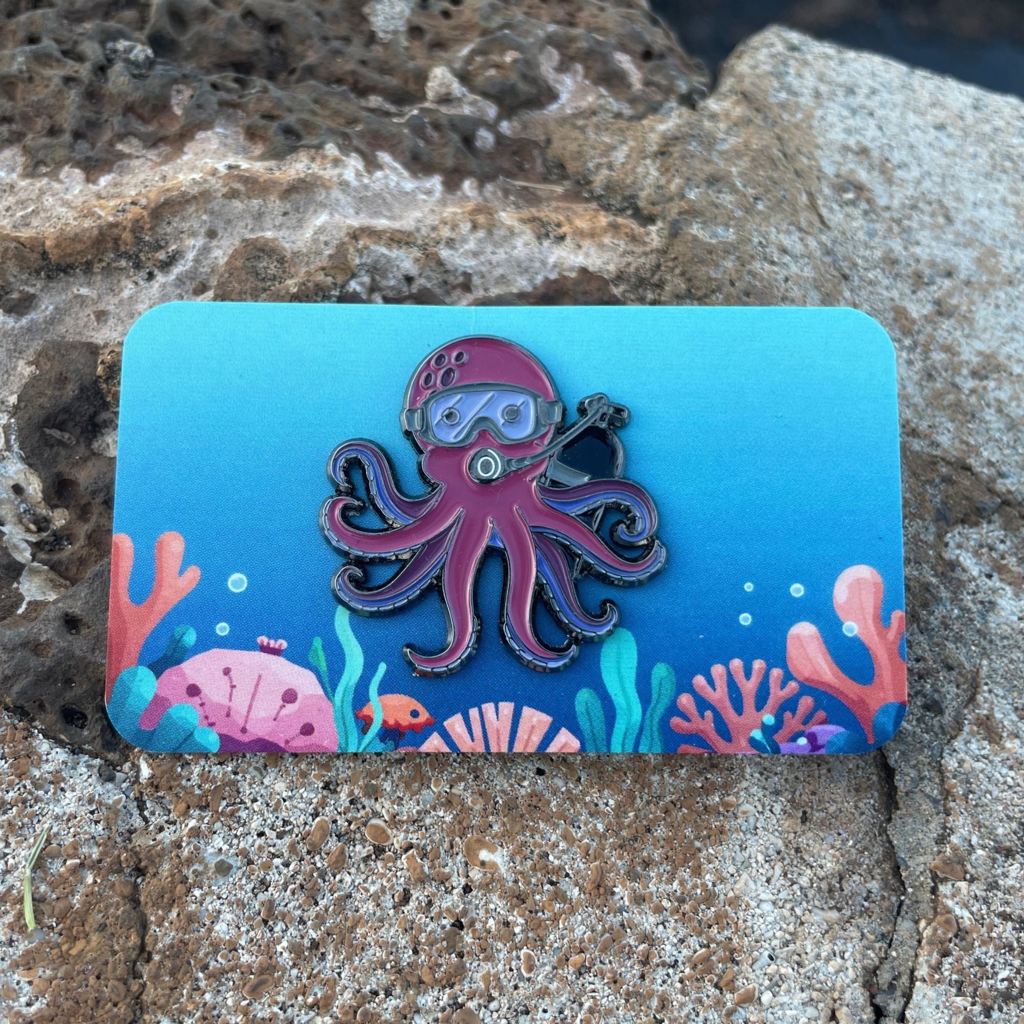 Purple octopus enamel pin on ocean themed backing card. Made by Golden Toad Studios, sold by Rinn Stitches