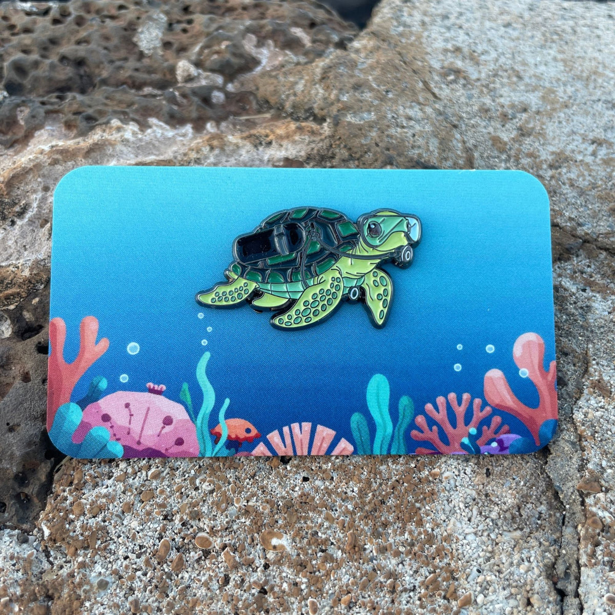 Sea Turtle scuba diver enamel pin on a colorful ocean themed backing card. Made by Golden Toad Studio, sold by Rinn Stitches